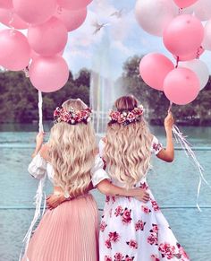 two girls are holding balloons in front of a fountain