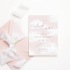 a pink and white wedding card with a bow on the front is laying next to it's envelope