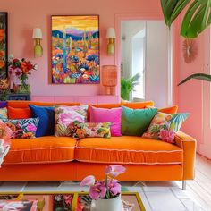 an orange couch with colorful pillows in a living room filled with pictures and flowers on the wall