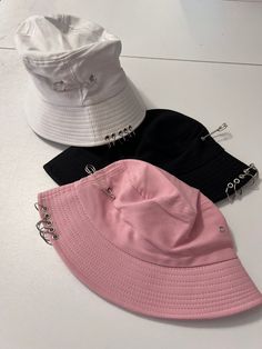 Pink black or white hat with safety pins and rings. Hella perfect for every day street wear!  Hats measure 23 inches and can be adjusted to be smaller, not bigger.  Note: please measure your head. I don't appreciate bad reviews from buyers who don't measure and who don't read the measurements.  Thank you in advance. Partnered design by Glitz & Candy Co.  Check them out on Facebook & Etsy! Drop-shipped by Glitz & Candy Co. Trendy Pink Hats For Music Festival, Trendy White Bucket Hat, Trendy Bucket Hat For Music Festival, Trendy Hats For Spring Music Festival, Adjustable Summer Rave Hats, Trendy Adjustable Bucket Hat For Music Festival, Trendy Adjustable Bucket Hat, Harajuku Style Adjustable Party Hat, Edgy Adjustable Snapback Hat