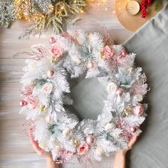 someone is holding a wreath with pink and white flowers on it next to other christmas decorations