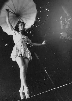 a black and white photo of a woman holding an umbrella while standing on a tightrope