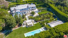 an aerial view of a large home surrounded by lush green trees and bushes, with a swimming pool in the foreground