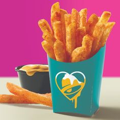 french fries in a blue container next to a bowl of dipping sauce on a pink and purple background