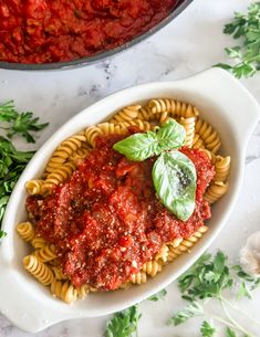 pasta with tomato sauce and basil leaves in a white bowl on a marble countertop