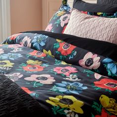 a bed with black and pink flowers on it's comforter, along with two pillows