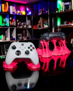 two video game controllers sitting next to each other on top of a glass table with neon lights behind them