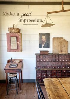 an old wooden desk and chair in a room with white walls, wood flooring and paintings on the wall