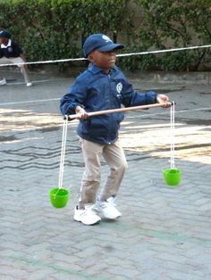 a young boy holding two plastic buckets on a rope with another child in the background