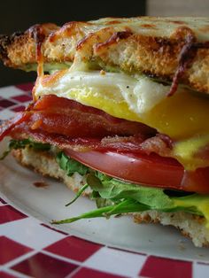 a bacon, egg and tomato sandwich is on a plate with a checkered tablecloth