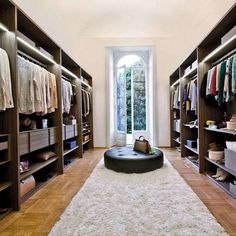 a large walk - in closet with lots of clothes on shelves and a round ottoman