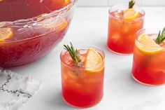 three glasses filled with red liquid and garnished with rosemary, sitting on a table