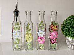 three empty glass bottles with flowers painted on them next to a potted green plant