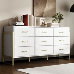 a white dresser with gold handles in a room next to a black lamp and rug