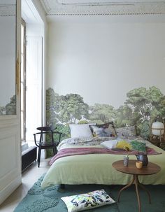 a bedroom with a green bed and wallpaper that has trees painted on the walls