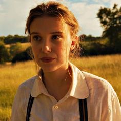 a woman standing in the middle of a field with her eyes closed and looking at the camera