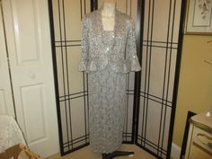 Stunning silver 2 piece dress by R & M Richards.  Silver/grey/pewter color with matching scattered sequins. The sheer stretchy lace is 55% polyester, 42% nylon, 3% spandex. The jacket is sheer and unlined. The tank dress is fully lined in stretchy 100% polyester. Hand wash. The dress has a back zip. Back vent. Scalloped hem. The jacket 3/4 bell sleeve jacket is gently ruffled and has a single hook closure at the waist. Size 6. The dress measures 49 1/2" long.  Laying flat seam to seam un-stretch Fitted Lace Mother Of The Bride Evening Dress, Lace Mother Of The Bride Dress With Sequins, Evening Fitted Sequined Mother Of The Bride Dress, Fitted Spring Mother Of The Bride Dress With Sequins, Fitted Sequin Mother Of The Bride Dress For Spring, Fitted Sequin Mother Of The Bride Dress For Party, Spring Lace Mother Of The Bride Dress With Sequins, Holiday Sequined Mother Of The Bride Dress, Formal Fitted Sequin Mother Of The Bride Dress