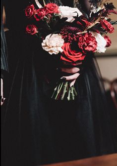 a woman in a black dress holding a bouquet of red and white flowers on her wedding day