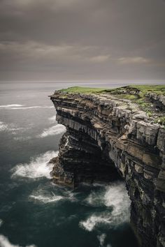 an ocean cliff with waves crashing against the rocks and grass growing on it's sides