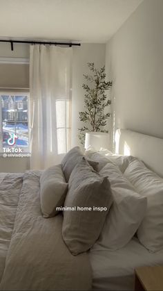 a bed with white sheets and pillows in a bedroom next to a window that has curtains on it