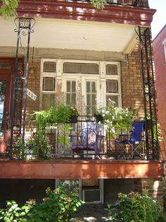 a balcony with chairs and plants on the balconies, in front of a brick building