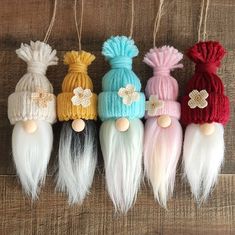 five different colored knitted hats hanging from strings on a wooden surface with white and red feathers