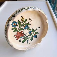 a bowl with flowers painted on it is sitting on a white countertop in front of a window