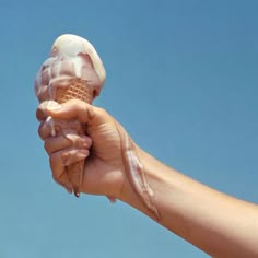 a hand holding an ice cream cone with icing on it against a blue sky