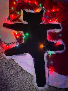 a cross with christmas lights around it on the floor in front of a bed sheet