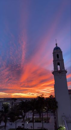 a clock tower is silhouetted against a colorful sky at dusk with palm trees in the foreground