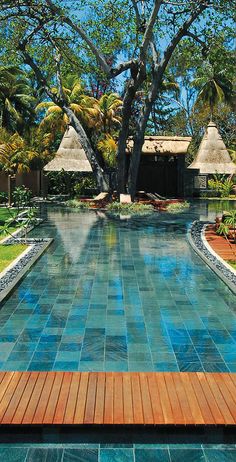 an outdoor swimming pool with wooden decking and trees in the backgrouds