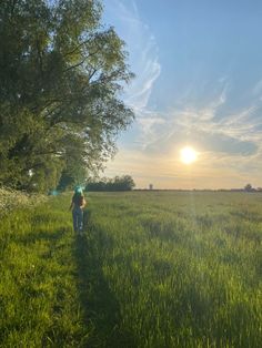 a person walking through the grass towards the sun