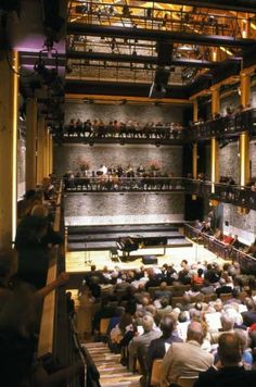 an auditorium filled with lots of people sitting on top of wooden steps and looking up at the stage