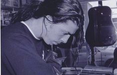 a young woman is looking at an old record player in her home studio, with the guitar behind her