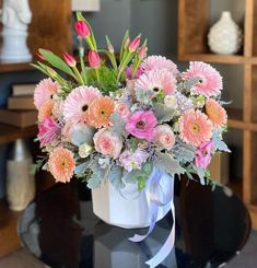 a white vase filled with pink flowers on top of a black table in a living room