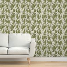 a white couch sitting in front of a wall with green trees on it and a wooden floor