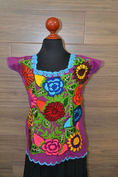 "This handmade Mexican shirt has been embroidered with beautiful colorful flowers. It will look great with any color skirt or pants. It has short sleeves and a scoop neckline. This is a nice comfortable casual cotton shirt. It is perfect as a gift for a friend or someone special. This shirt is a medium size. It measures 19\" wide x 23\" long. It has 7\" sleeve openings and a 8\" opening for the neck. Size Medium About Our Items: Each one of our items is handmade/hand woven by Indigenous communit Purple Embroidered Top With Floral Embroidery For Summer, Purple Floral Embroidered Top For Summer, Embroidered Bohemian Purple Blouse, Bohemian Embroidered Purple Blouse, Purple Embroidered Bohemian Blouse, Bohemian Purple Embroidered Blouse, Bohemian Purple Blouse With Floral Embroidery, Purple Bohemian Top With Floral Embroidery, Bohemian Purple Top With Floral Embroidery