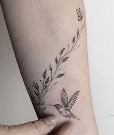 a woman's arm with a small bird and flower tattoo on the left side