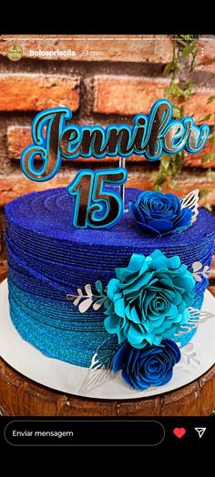 a cake with blue frosting and flowers sitting on top of a wooden table next to a brick wall