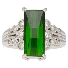 This stunning ring features a vivid green checkerboard-cut 3.19 CT tourmaline stone set on a platinum 900 band. The center stone is complimented by 0.27 Ct round-cut diamonds on either side of the shank. Size 6 and adjustable. The vintage feel of this ring makes a statement, one of class and appreciation of the beautiful finer things in life. Details: Item Type: Vintage Ring Metal: Platinum 900 Size: 6 (adjustable) Weight: 10.98 Grams Setting: Filigree, Prong, Milgrain Center Stone Details: Stone Type: Indicolite Tourmaline Carat: 3.19 Cut: Checkerboard Color: Green Measurements: 14.2 x 6.4 x 3.95 mm Side Stones Details: Type: Diamond Cut: Round Carat: 0.27 Color: H-I Clarity: SI1-SI2 Sapphire Cocktail Ring, Indicolite Tourmaline, Vintage Cocktail Ring, Gold Cocktail Ring, Gold Cocktail, Tourmaline Stone, Filigree Ring, Art Deco Diamond, Garnet Rings