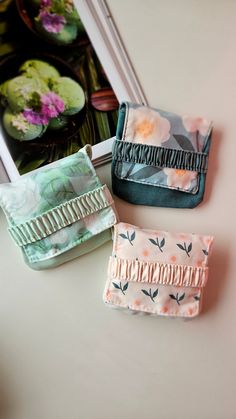 three small purses sitting on top of a table next to a book and flowers