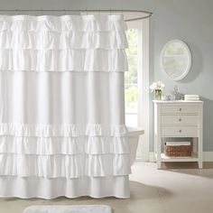 a white shower curtain with ruffles on the bottom is in front of a window