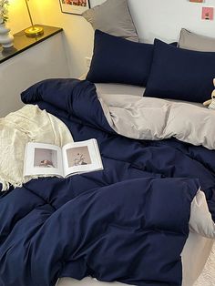 an unmade bed with blue comforter and two stuffed animals on the floor next to it