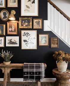 a bunch of pictures are hanging on the wall above a wooden table and bench in front of a staircase