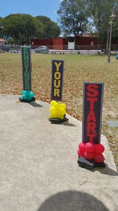 some signs that are sitting in the grass near each other on a cement slab, with one sign reading your start