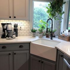 a white kitchen sink sitting under a window next to a potted plant and coffee maker