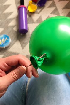 a person is holding a green balloon with a pin in it's middle and several other items on the floor