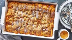 a casserole dish filled with bread and covered in powdered sugar next to a cup of coffee