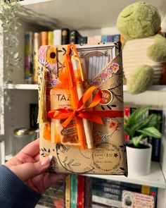 a person holding up a gift wrapped in brown paper with orange ribbon and bows on it