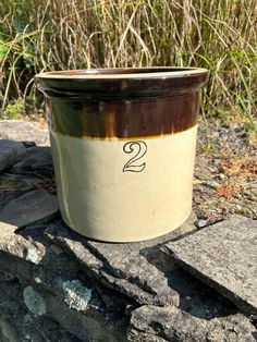 a brown and white pot sitting on top of a rock next to some grass with the number two written in it